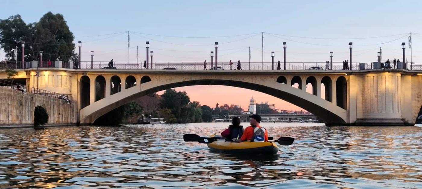 Two people kayaking under a bridge on the Guadalquivir in Seville